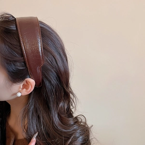 Detail of brown pleated leather headband showing stitching and glossy finish texture