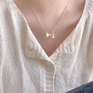 Close-up of elegant gold bow pendant necklace worn by model against knit sweater