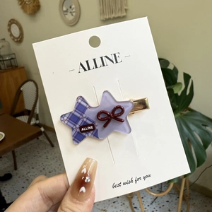 Star-shaped purple plaid hair clip with a red bow tie on a white display card