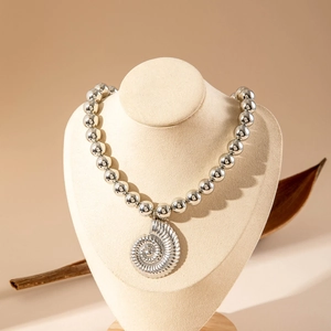Detail of silver beaded necklace with shell pendant on beige jewelry mannequin display