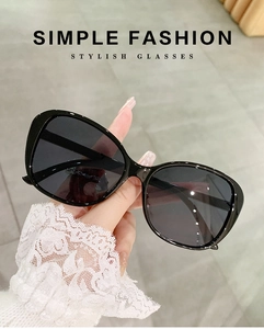 Person holding oversized black fashion sunglasses with a sleek arc frame design