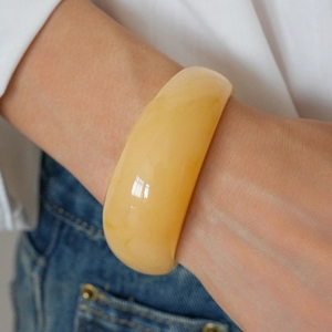 Close-up of yellow resin wide bangle with amber texture on person wearing a white shirt