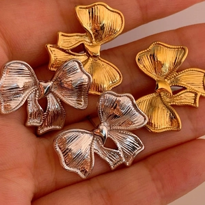Bow-knot earrings in gold and silver finish with textured patterns on a hand palm