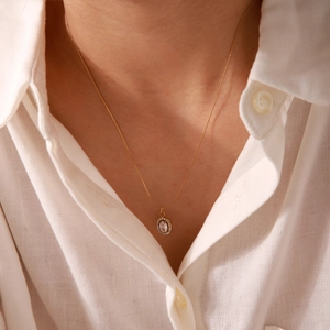 Close-up of 18K gold stainless steel necklace with oval pendant on a model wearing white shirt