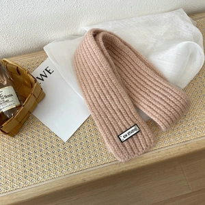Detailed texture of thick beige knit scarf with a woven label on a rustic background