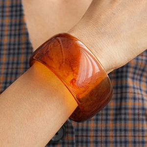 Detail of amber translucent resin bangle with natural swirl texture on plaid sleeve
