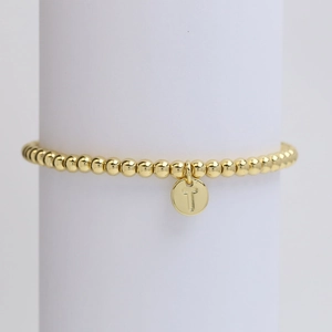 Detail of golden beaded bracelet featuring a round pendant engraved with letter T