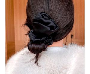 Detail of a large black satin silk scrunchie worn on long hair for a retro elegant look