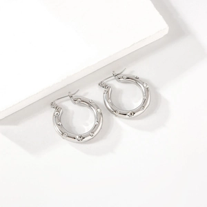 Polished silver stainless steel hoop earrings with crystals on a stone display base