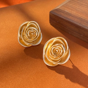 Vintage 3D gold rose flower stud earrings with detailed petal texture on orange background