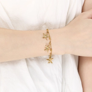 Close-up of a gold starfish charm bracelet on a wrist with beach holiday ocean vibes
