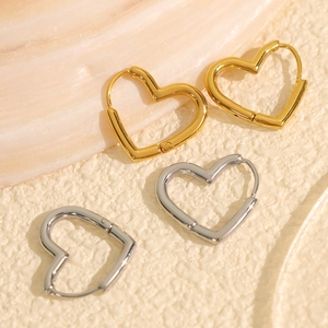Classic gold and silver stainless steel heart hoop earrings on a textured stone surface