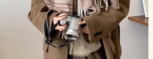 Detail of a brown plaid scarf with tassels paired with a thick wool coat for winter outfit