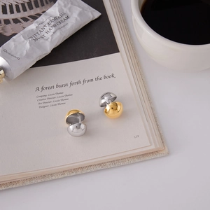 Detail of two-tone gold and silver dome earrings on an open book with coffee