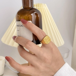 Detail of a gold square signet ring featuring a textured relief surface on a model's finger