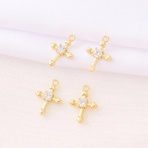 Macro shot of four golden cross charms with inset diamond crystals on white fabric