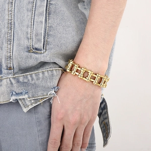 Detail of a gold stainless steel bike chain bracelet worn by a model in casual denim