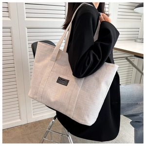 Detail of woven beige tote bag with black shoulder straps shown in office setting