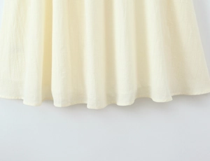 Detail eines beigen Puffärmel-Kleides mit Leinenstruktur und Falten am Saum