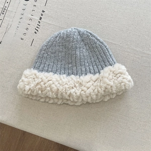 Detail of grey ribbed knit beanie with white faux fur trim on a textured background