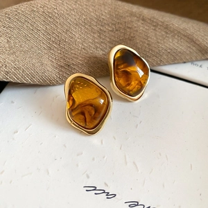 Macro shot of irregular amber stud earrings with elegant gold metal edges on textured paper