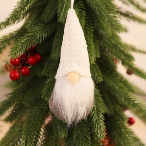 Close-up of a white knitted Christmas gnome hanging on a pine branch with red berries