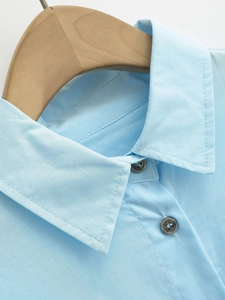 Detailed close-up of light blue shirt collar with dark grey buttons on a wooden hanger