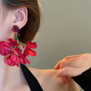 Close-up of red fabric flower drop earrings with green bead accents on a model
