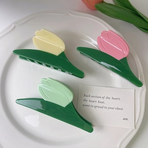 Three tulip hair claws in yellow pink and green flower designs on a white plate