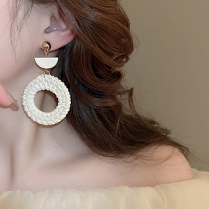 Detailed close-up of Bohemian straw woven circular earrings on a female model