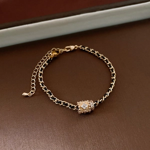 Detailed close-up of gold chain bracelet with woven cord and zircon cylinder pendant