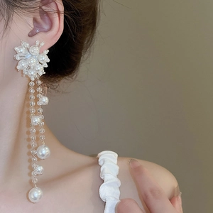 Detail of elegant long tassel earrings with white pearls and crystals on a model
