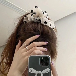 White heart print scrunchie hair tie with black piping shown in a mirror selfie hairstyle