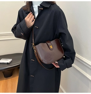 Detail of vintage dark brown saddle bag with shiny leather and gold twist lock clasp