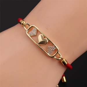 Macro detail of red string bracelet with gold heart charms and pavé zircon stones on wrist