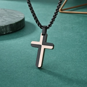 Two-tone stainless steel cross pendant necklace in black and rose gold on green surface