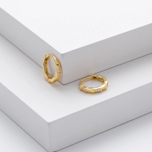 Detailed close-up of golden bamboo joint hoop earrings with white zircon on white steps
