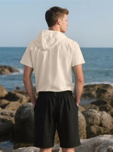 Rear view of men's summer linen set with beige hooded shirt and black shorts on beach