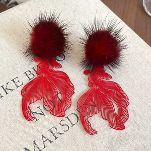 Detail of red hollow koi fish pendant with plush ball earring on a book background
