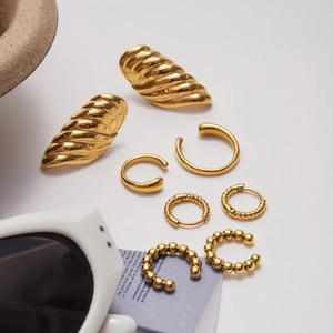 Set di quattro paia di orecchini a cerchio dorati e ear cuff su uno sfondo bianco pulito