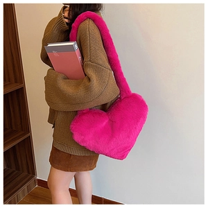 Close-up of heart-shaped pink faux fur shoulder bag worn by model in cozy interior