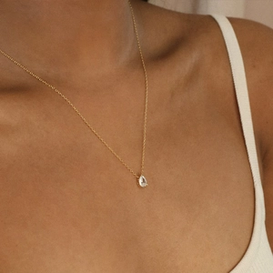Detail shot of a pear-shaped zircon pendant on a gold chain necklace worn by a model