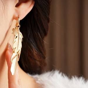 Close-up of golden feather earrings with moonstone pendant and micro-diamond accents