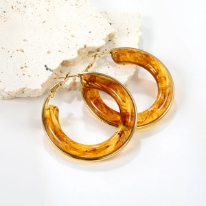Fashionable amber resin hoop earrings with golden metallic clasp on natural stone background