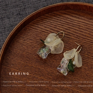 Detailed close-up of floral fabric earrings with pearls and iridescent pendants on wood