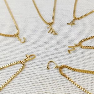 Gros plan de colliers en acier titane doré avec pendentifs initiales sur chaînes box