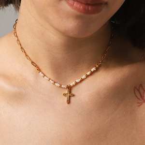 Close-up of a gold cross pendant necklace with white pearls and paperclip chain