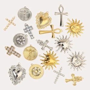 Variety of gold and silver stainless steel sun, heart, and cross charms on beige background