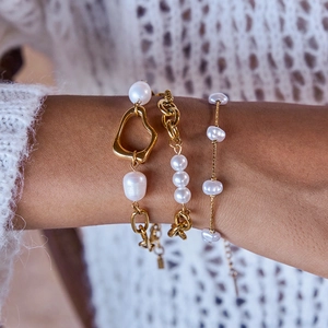 Close-up of gold layered bracelets with pearls and bow charms on a model's wrist