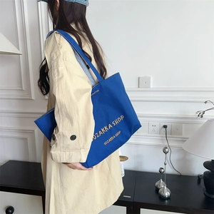 Blaue Canvas-Tasche mit gelber Stickerei, getragen von einem Model im beigen Trenchcoat